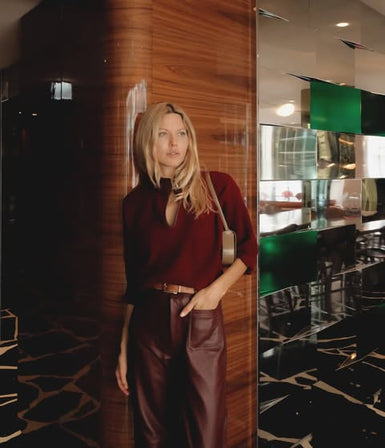 L’influenceuse Amandine Elina en pull cachemire et pantalon cuir bordeaux MAX&MOI, dans un hall d’hôtel.